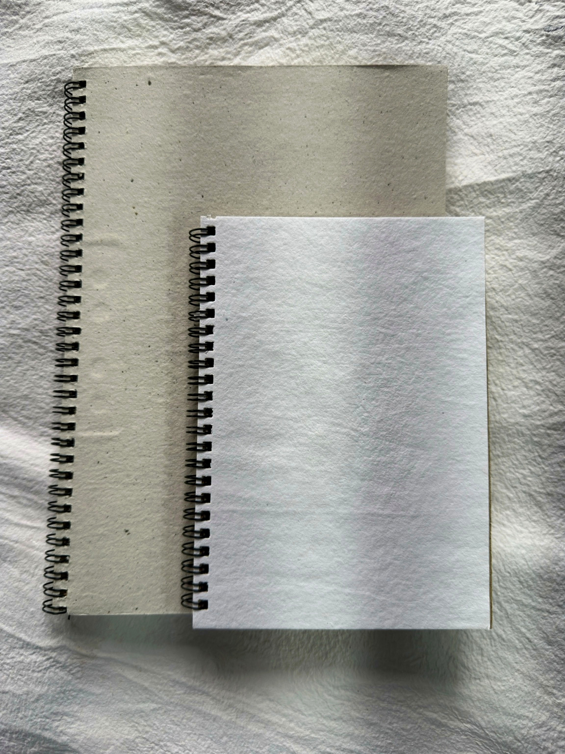 Two handmade paper notebooks, one large and one small, seen from above